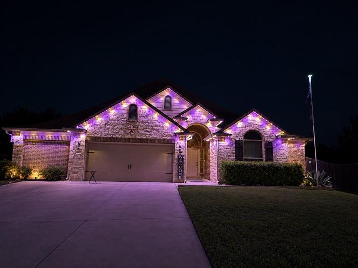 Purple and gold game day lighting on a stone and brick home