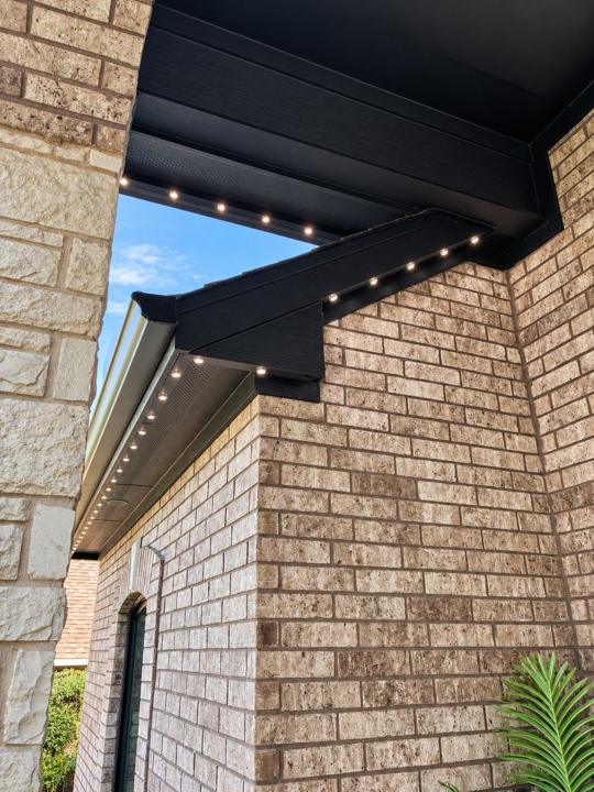 Low-profile lighting track set into a black soffit above a brick wall